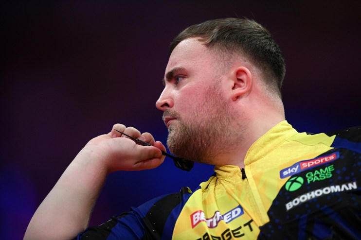 A male darts player in a yellow and blue shirt holding a dart, focused on his throw.
