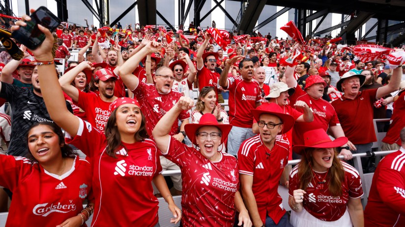 Jubilant Liverpool FC fans in red jerseys and hats cheering at a stadium during a match