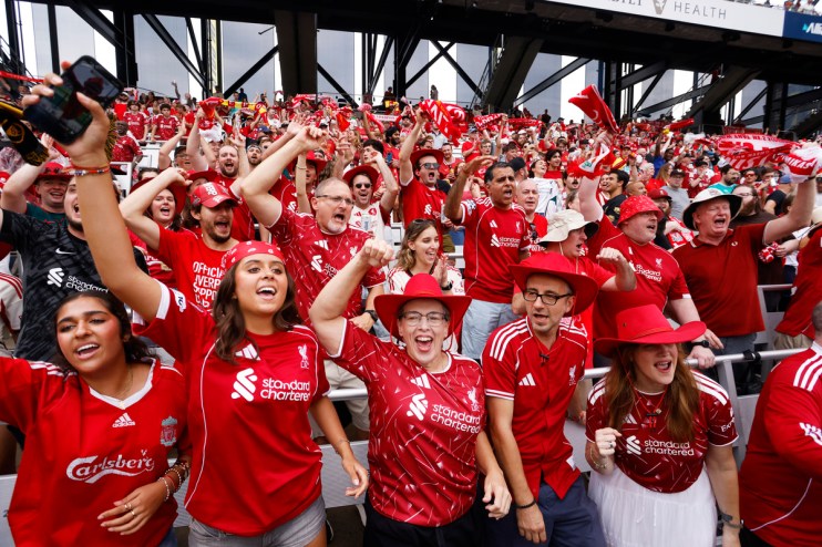 Jubilant Liverpool FC fans in red jerseys and hats cheering at a stadium during a match