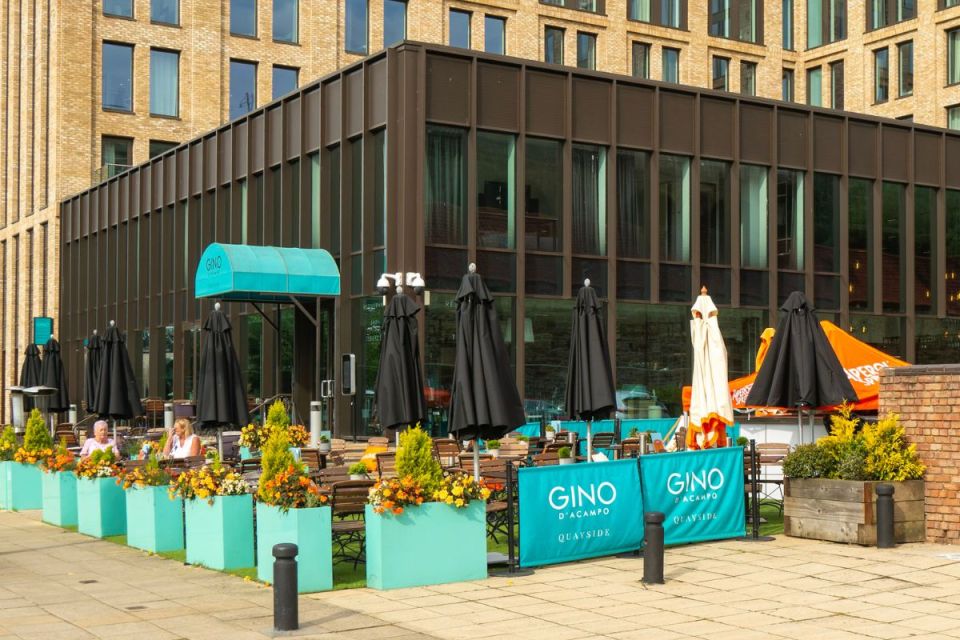 Gino DAcampo restaurant exterior with outdoor seating, teal planters, black umbrellas, and brick building