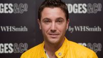 Gino DAcampo, smiling in a bright yellow jacket, against a dark background with GES & CO and WHSmith logos
