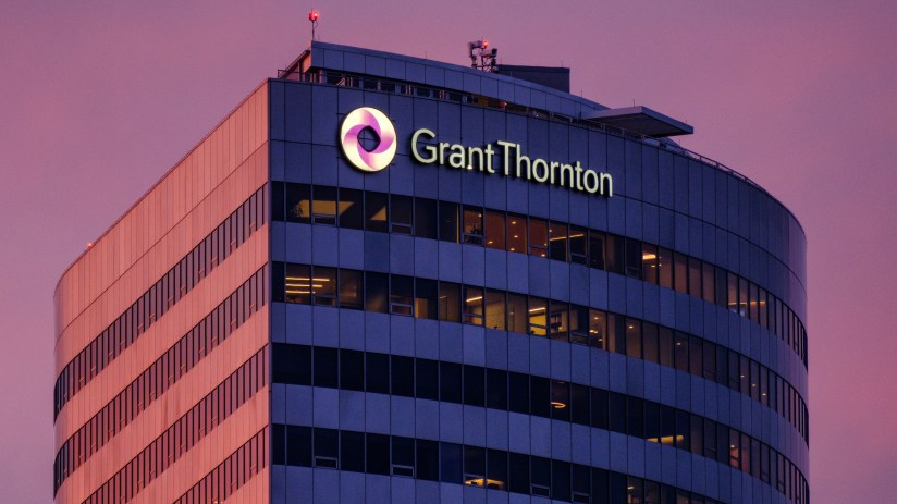 Grant Thornton building exterior with illuminated logo and name against a dramatic pink and purple sky at dusk.