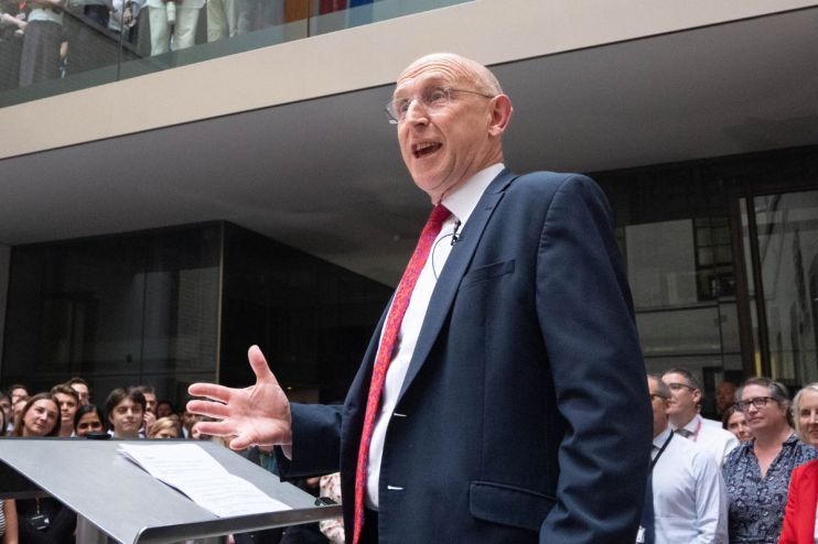 Man in suit and red tie speaking at a podium to an audience in a modern building.