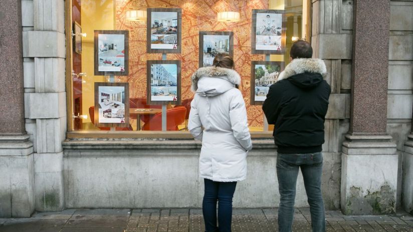 Two people looking at real estate listings in an estate agents window, showcasing properties for sale.