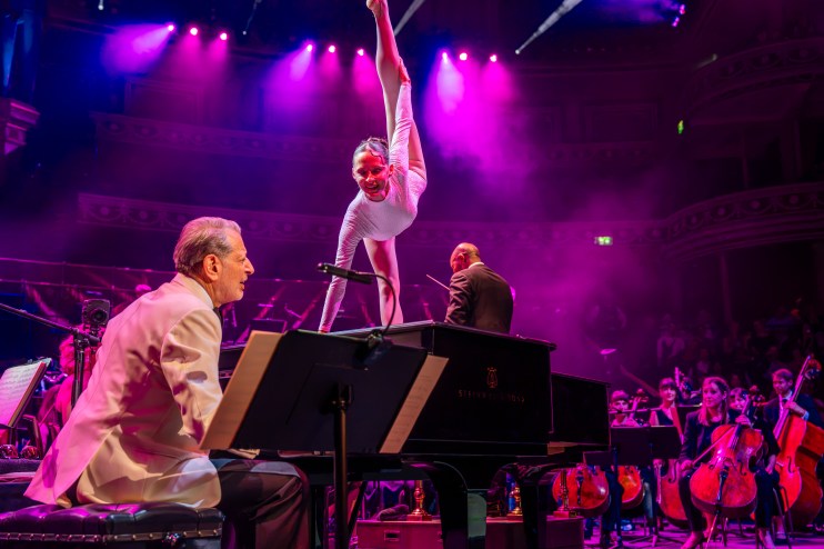 Carsten Windhorst performing with a gymnast, pianist, and orchestra under purple lights.