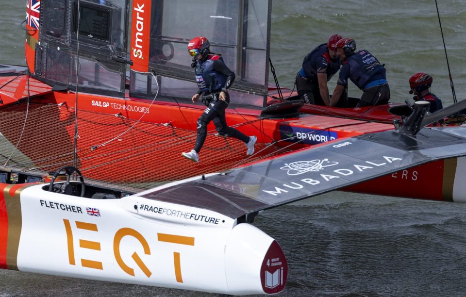 SailGP catamaran with crew members, one running across the deck, others working on the boat.