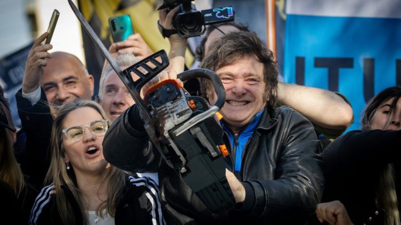 Javier Milei delivering a passionate speech at a political rally, gesturing emphatically with supporters in the background