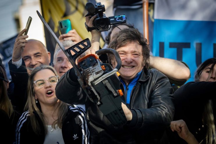 Javier Milei delivering a passionate speech at a political rally, gesturing emphatically with supporters in the background