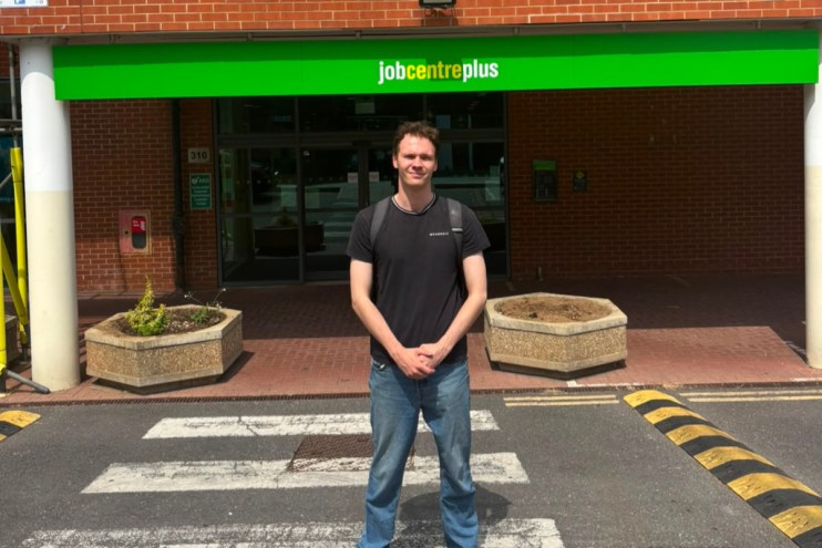 Young man in front of a Jobcentre Plus building, standing on a pedestrian crossing.