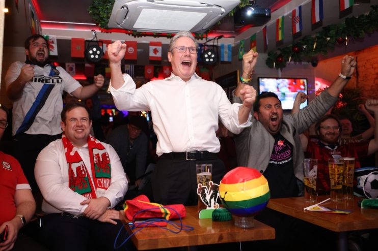 Keir Starmer holding a football with a World Cup logo, smiling and engaging in a sports event discussion.