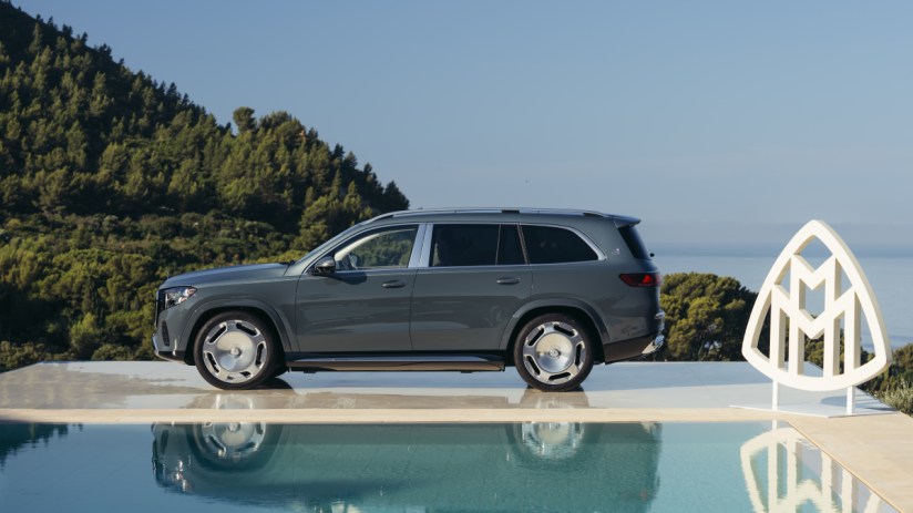 Gray Mercedes-Maybach GLS SUV parked next to a pool with a Maybach logo, green hills, and ocean in background