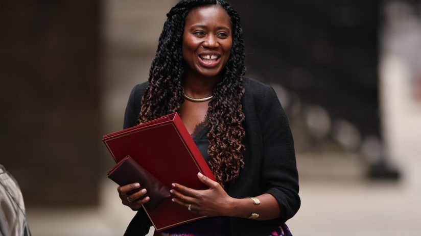 Miatta Fahnbulleh, director of New Economics Foundation, smiling and holding red documents, wearing a black blazer.
