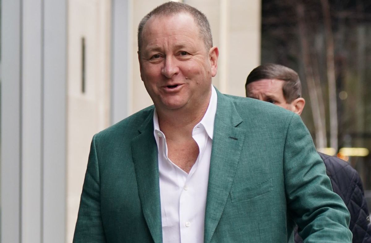 Mike Ashley in a business suit at a corporate event, discussing strategic plans, surrounded by executives and media personnel