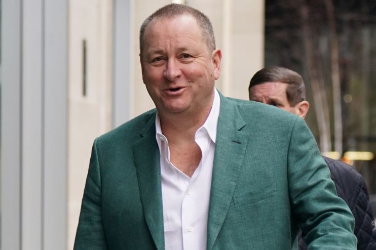 Mike Ashley in a business suit at a corporate event, discussing strategic plans, surrounded by executives and media personnel
