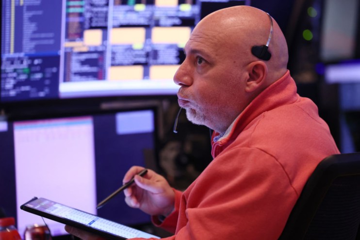 Stock trader with headset and tablet monitors market data, reflecting Nasdaq, NYSE correction concerns.