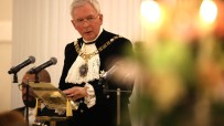 Nicholas Lyons, former Lord Mayor of London, speaking at a podium with microphones, discussing fresh ISA rules.