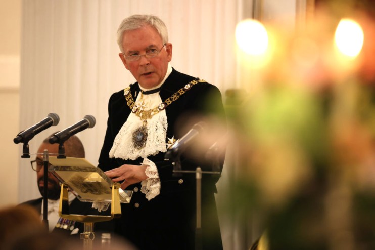 Nicholas Lyons, former Lord Mayor of London, speaking at a podium with microphones, discussing fresh ISA rules.