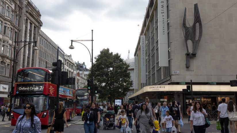 Bustling Oxford Street with shoppers, iconic red buses, and storefronts under a clear sky in a vibrant urban scene