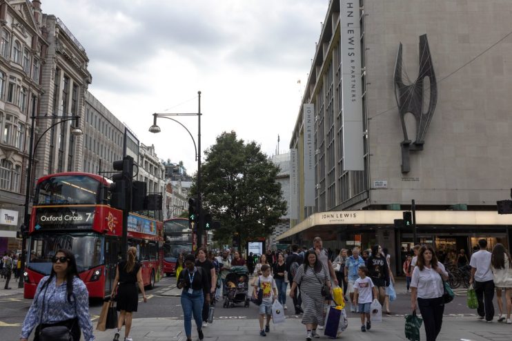 Bustling Oxford Street with shoppers, iconic red buses, and storefronts under a clear sky in a vibrant urban scene