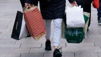 Shoppers carrying various retail bags, including New Look and M&S Food, on a paved street, indicating retail sales activity.