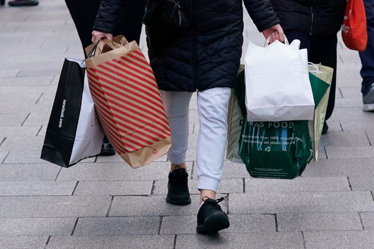 Shoppers carrying various retail bags, including New Look and M&S Food, on a paved street, indicating retail sales activity.