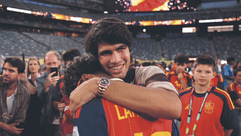Carlos Alcaraz embracing a person, smiling, wearing a Rolex Daytona Rainbow watch at a stadium event