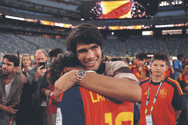Carlos Alcaraz embracing a person, smiling, wearing a Rolex Daytona Rainbow watch at a stadium event