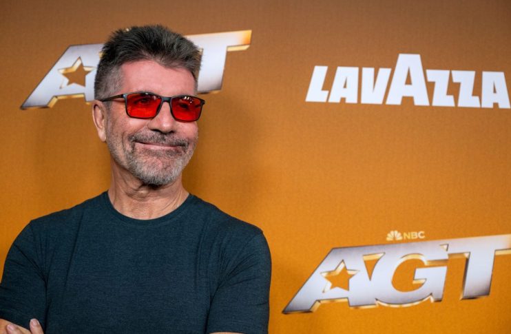 Simon Cowell smiling brightly during a press event, dressed in a classic tailored suit, showcasing his signature confident...