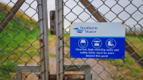 Southern Water safety sign on a chain link fence, detailing required PPE like hard hats and safety boots.