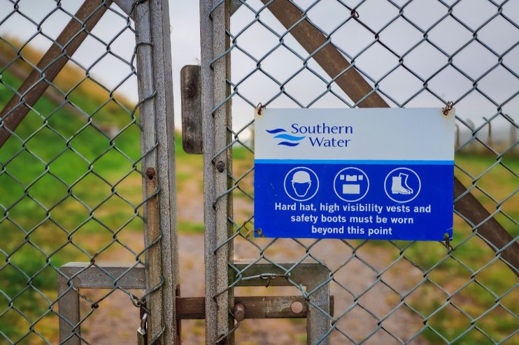 Southern Water safety sign on a chain link fence, detailing required PPE like hard hats and safety boots.