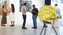 Art enthusiasts view colorful abstract paintings and a unique yellow light sculpture at a Square Mile art gallery.