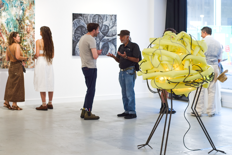 Art enthusiasts view colorful abstract paintings and a unique yellow light sculpture at a Square Mile art gallery.