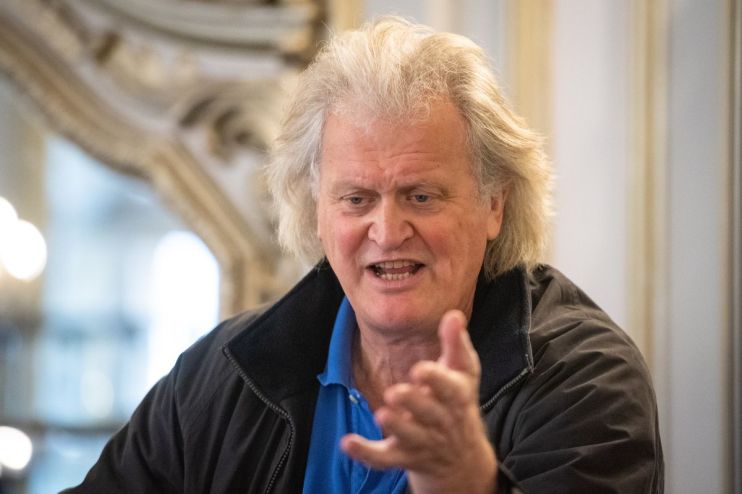 Tim Martin, founder of JD Wetherspoon, speaking and gesturing with an open hand, wearing a blue polo shirt and dark jacket.