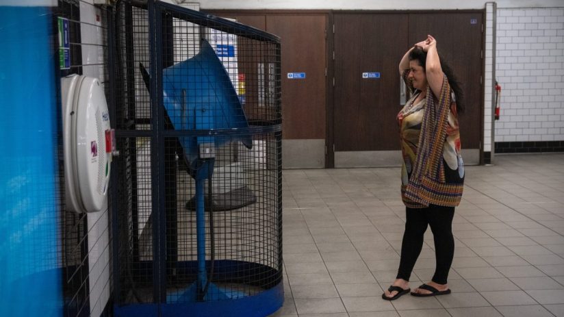 Crowded London Underground platform during summer heat wave, passengers fanning themselves to stay cool