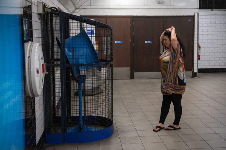 Crowded London Underground platform during summer heat wave, passengers fanning themselves to stay cool