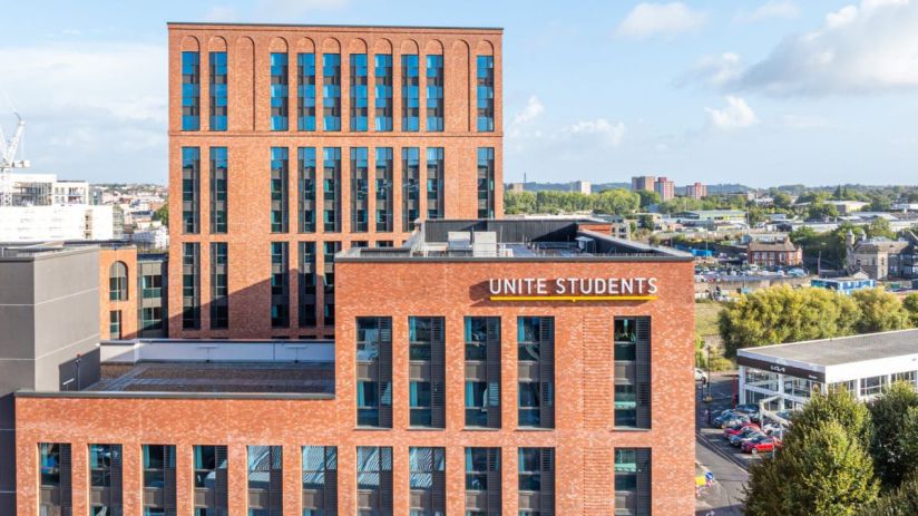 Unite Students building with brick facade and blue windows, city skyline in background under blue sky