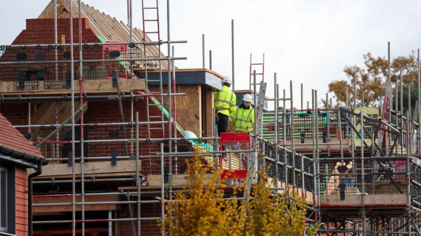 Construction workers in hard hats and high-vis jackets on scaffolding around a Vistry housing development.