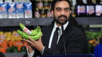 Zohran Mamdani, a man with a beard, holds a bunch of green bananas with a 30% off label at a grocery store.
