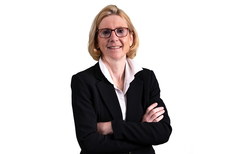 Christiane Hoffmann, a blonde woman in glasses and a black business suit, smiling with arms crossed.