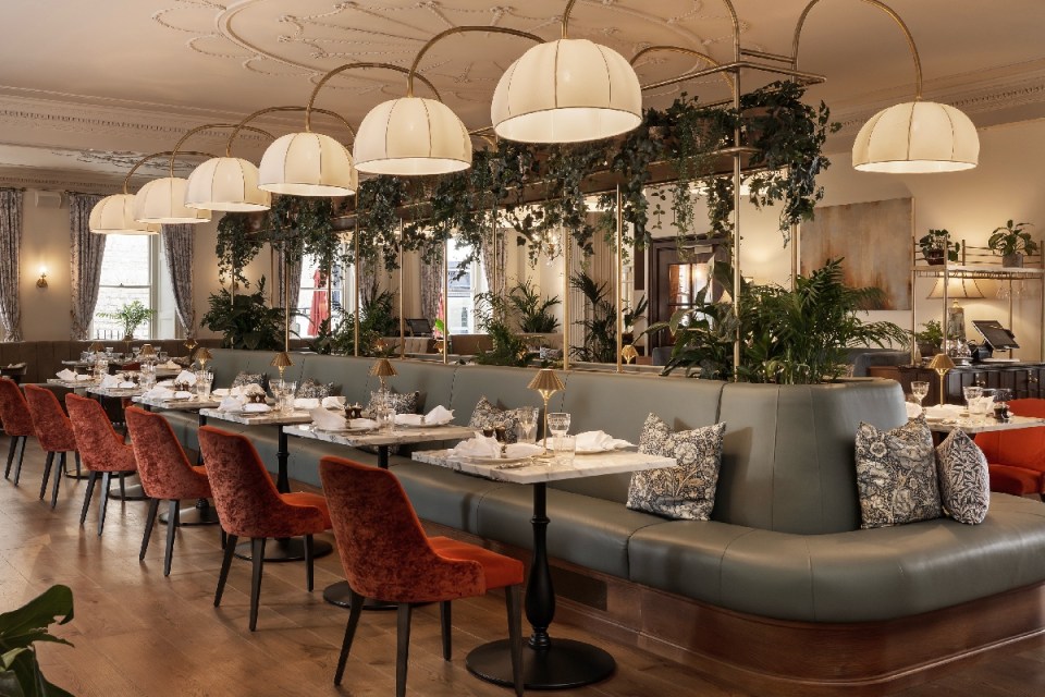 Elegant dining room at Francis Hotel Bath Emberwood, featuring green banquettes, marble tables, and velvet chairs.