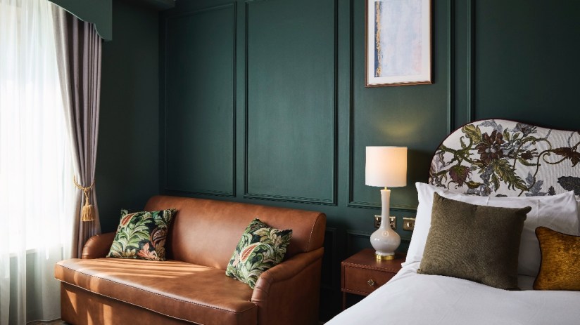 Elegant Francis Hotel Bath guest room with dark green paneled walls, brown leather sofa, and floral headboard.