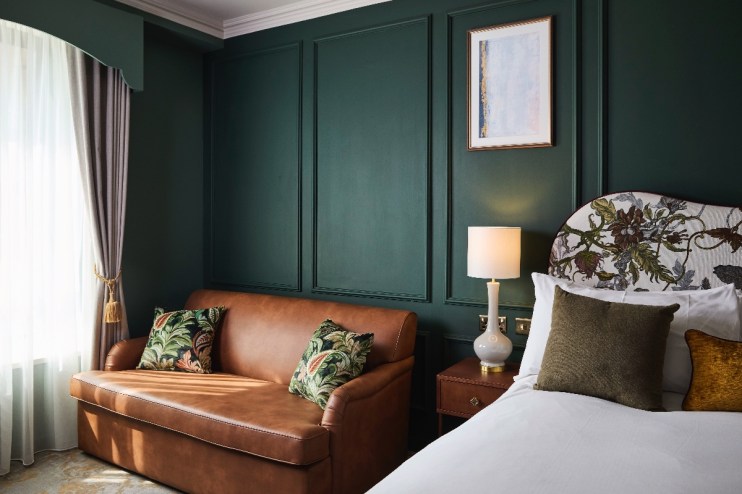 Elegant Francis Hotel Bath guest room with dark green paneled walls, brown leather sofa, and floral headboard.