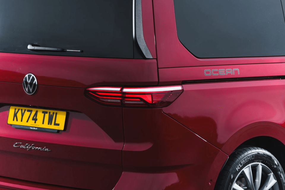 Rear view of a red Volkswagen California Ocean camper van, showing the taillight, VW logo, and license plate.