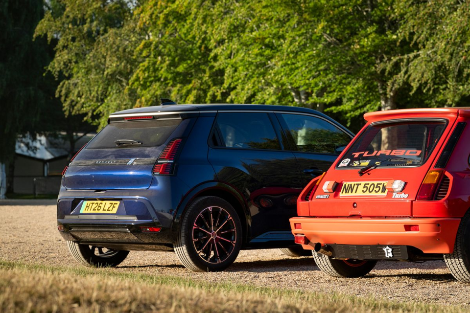 Rear view of a blue Renault 5 E-Tech and an orange Renault 5 Turbo parked outdoors on gravel.