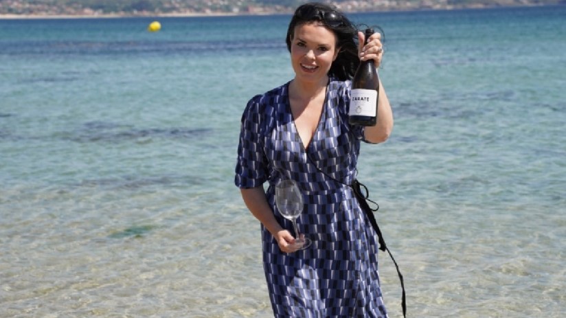 Libby Albarino holding a bottle of Zarate wine and a glass by the ocean