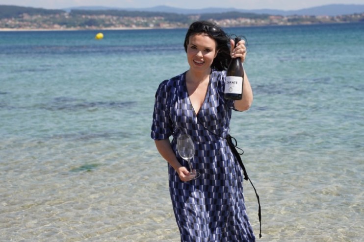 Libby Albarino holding a bottle of Zarate wine and a glass by the ocean