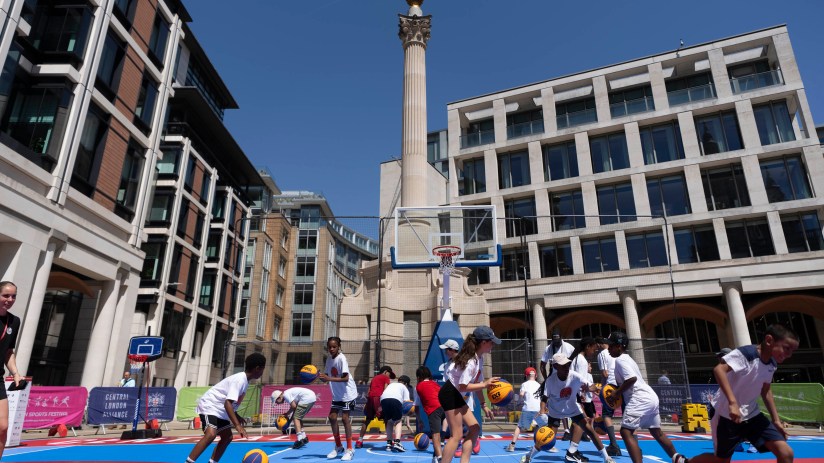 Kids playing basketball at a pop-up court in London, with the Monument to the Great Fire visible.