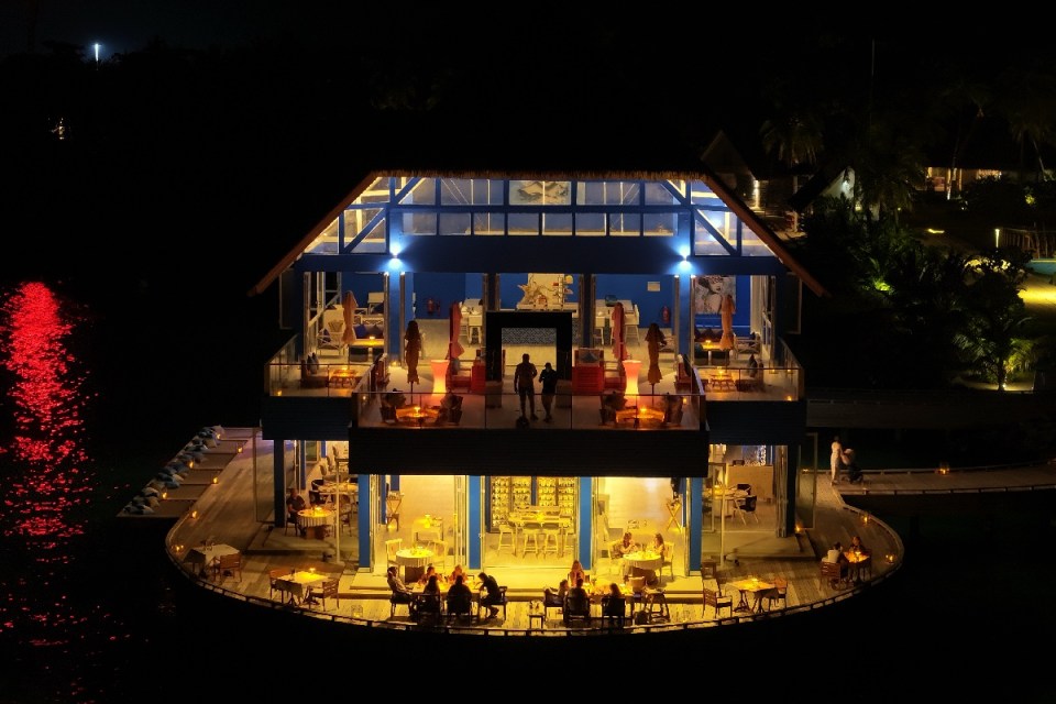 Maldives Ifuru resort restaurant and bar illuminated at night, with patrons dining on overwater decks.