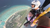 Two people skydiving over the Maldives, with turquoise water, coral reefs, and an island resort below.