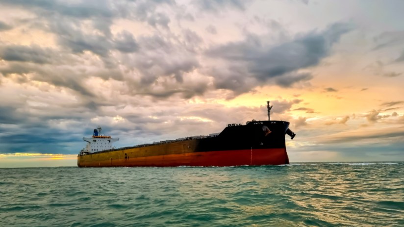 Large oil tanker navigating a strait under a cloudy sky, impacting oil prices and global trade.